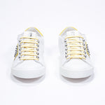 Front view of low top white and yellow sneaker. Full leather upper with studs and white rubber sole.