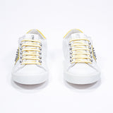 Vue de face d'un modèle bas blanc et jaune sneaker. Tige en cuir avec clous et semelle en caoutchouc blanc.