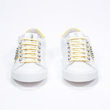 Front view of low top white and yellow sneaker. Full leather upper with studs and white rubber sole.