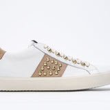 Side profile of low top white and cuoio sneaker. Full leather upper with studs and vintage rubber sole.