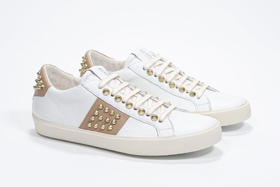 Three quarter front view of low top white and cuoio sneaker. Full leather upper with studs and vintage rubber sole.