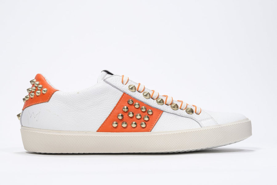 Side profile of low top white and orange sneaker. Full leather upper with studs and vintage rubber sole.