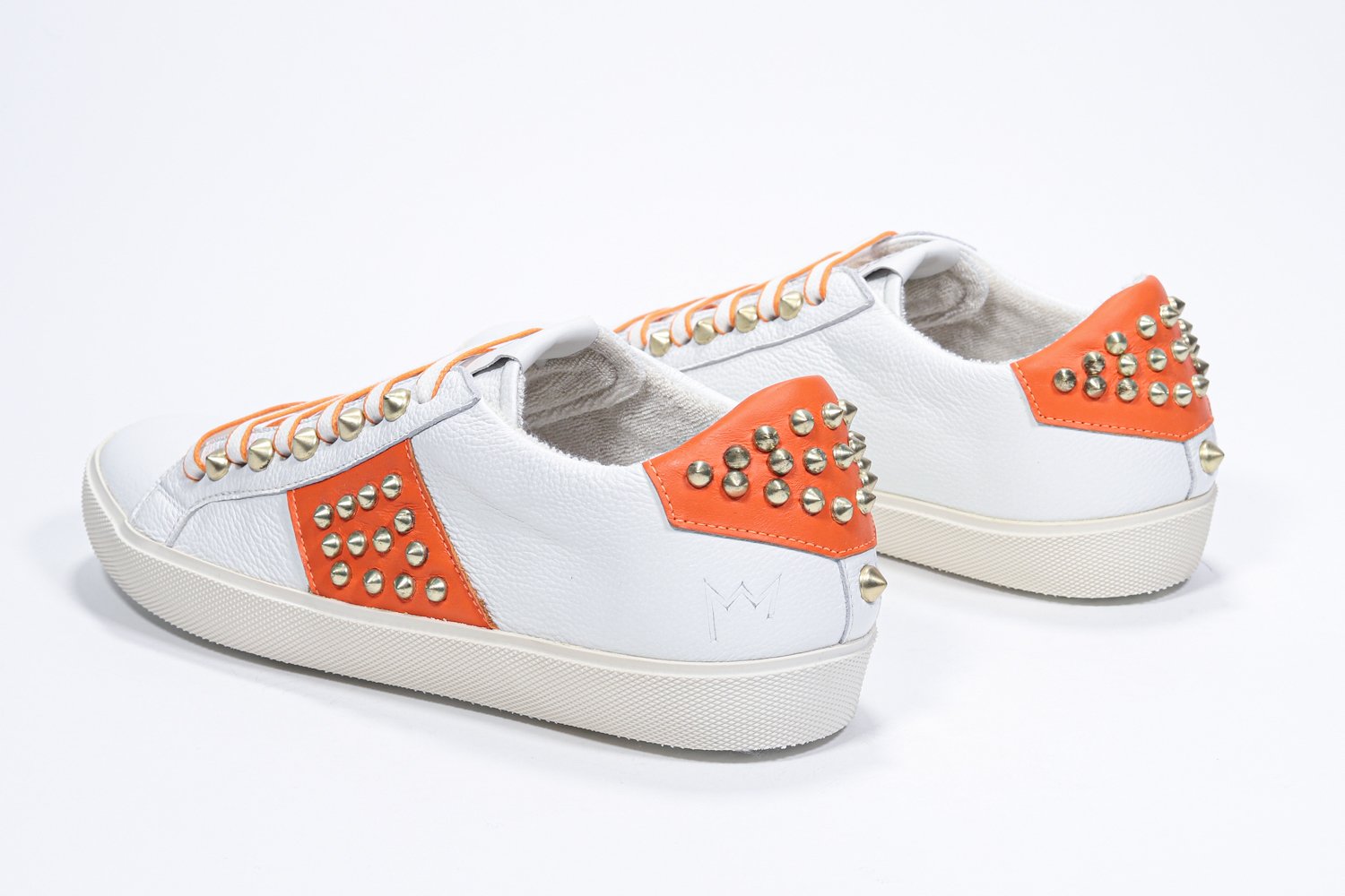 Three quarter back view of low top white and orange sneaker. Full leather upper with studs and vintage rubber sole.