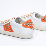 Three quarter back view of low top white and orange sneaker. Full leather upper with studs and vintage rubber sole.