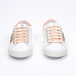 Front view of low top white and orange sneaker. Full leather upper with studs and vintage rubber sole.