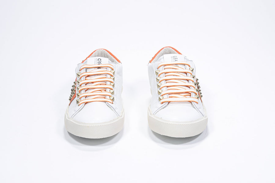 Front view of low top white and orange sneaker. Full leather upper with studs and vintage rubber sole.