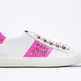 Side profile of low top white and neon pink sneaker. Full leather upper with studs and white rubber sole.