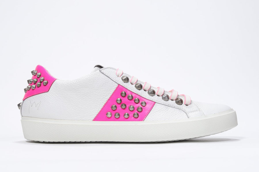 Side profile of low top white and neon pink sneaker. Full leather upper with studs and white rubber sole.