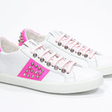 Three quarter front view of low top white and neon pink sneaker. Full leather upper with studs and white rubber sole.