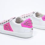 Three quarter back view of low top white and neon pink sneaker. Full leather upper with studs and white rubber sole.
