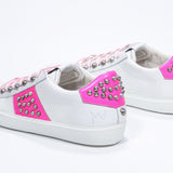 Three quarter back view of low top white and neon pink sneaker. Full leather upper with studs and white rubber sole.