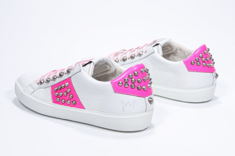 Three quarter back view of low top white and neon pink sneaker. Full leather upper with studs and white rubber sole.