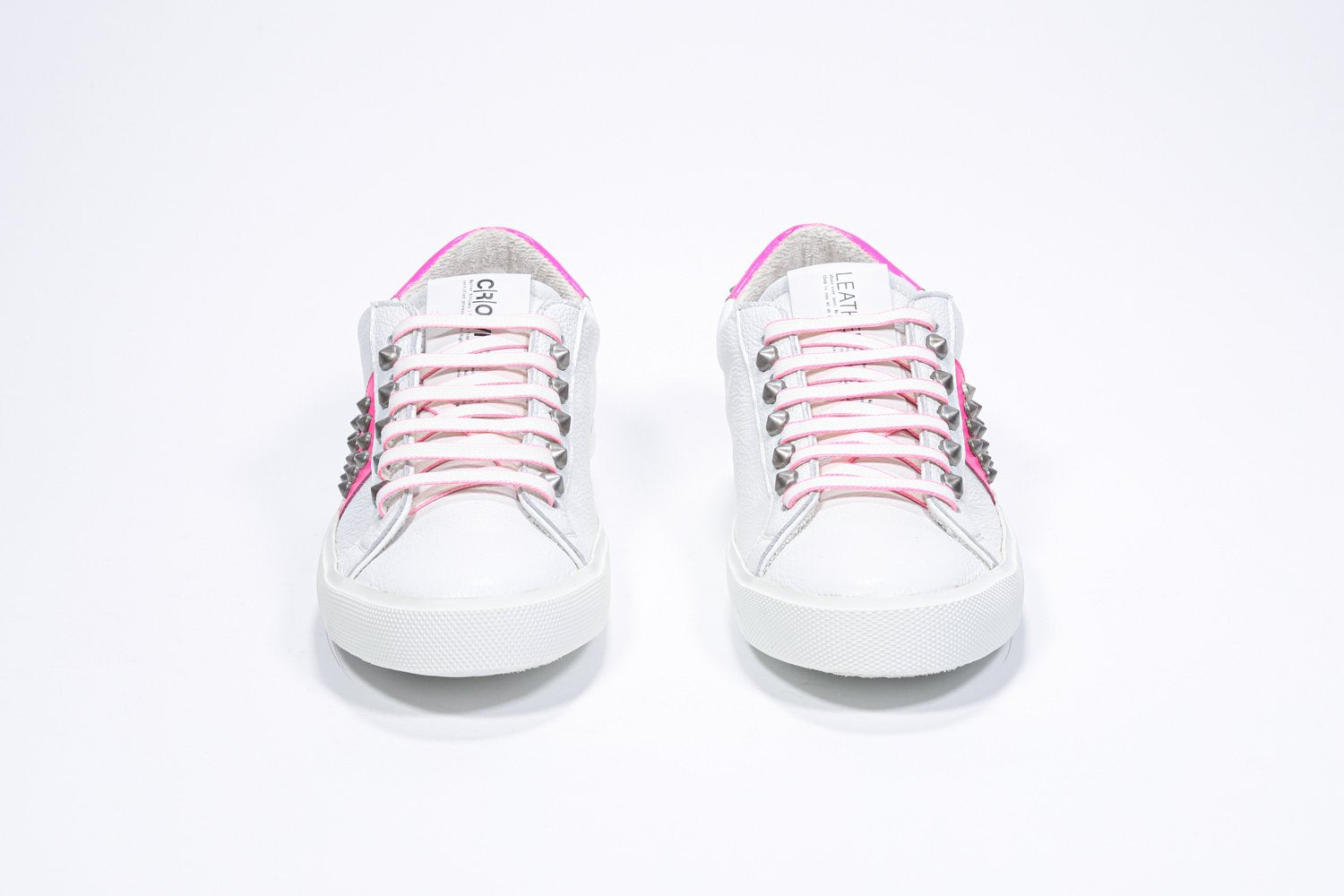 Front view of low top white and neon pink sneaker. Full leather upper with studs and white rubber sole.