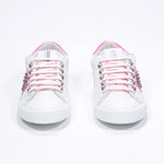 Front view of low top white and neon pink sneaker. Full leather upper with studs and white rubber sole.