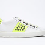 Side profile of low top white and neon yellow sneaker. Full leather upper with studs and white rubber sole.