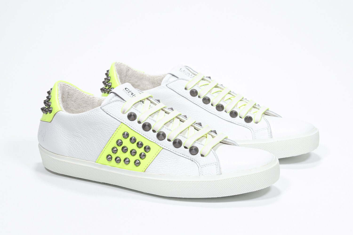 Three quarter front view of low top white and neon yellow sneaker. Full leather upper with studs and white rubber sole.