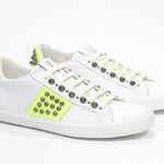 Three quarter front view of low top white and neon yellow sneaker. Full leather upper with studs and white rubber sole.