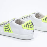 Three quarter back view of low top white and neon yellow sneaker. Full leather upper with studs and white rubber sole.