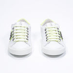 Front view of low top white and neon yellow sneaker. Full leather upper with studs and white rubber sole.