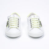 Front view of low top white and neon yellow sneaker. Full leather upper with studs and white rubber sole.