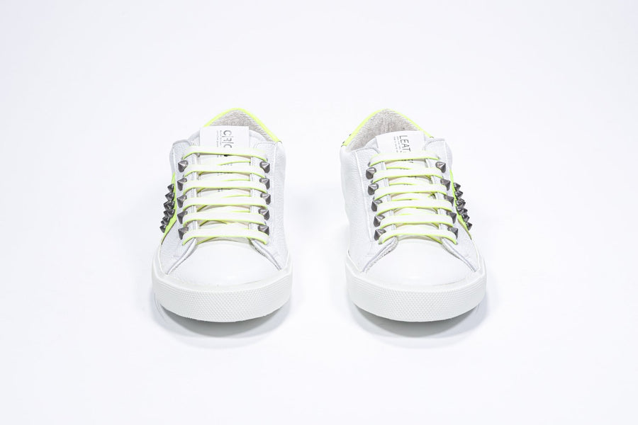 Front view of low top white and neon yellow sneaker. Full leather upper with studs and white rubber sole.
