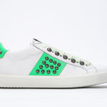 Side profile of low top white and neon green sneaker. Full leather upper with studs and white rubber sole.