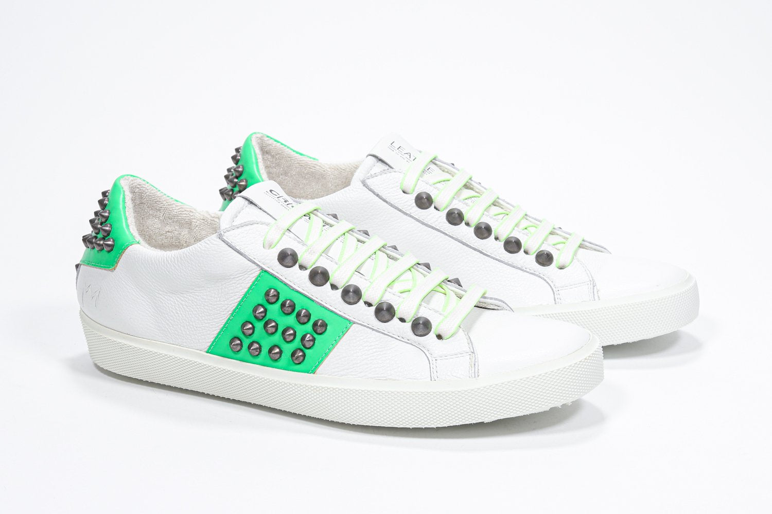 Three quarter front view of low top white and neon green sneaker. Full leather upper with studs and white rubber sole.