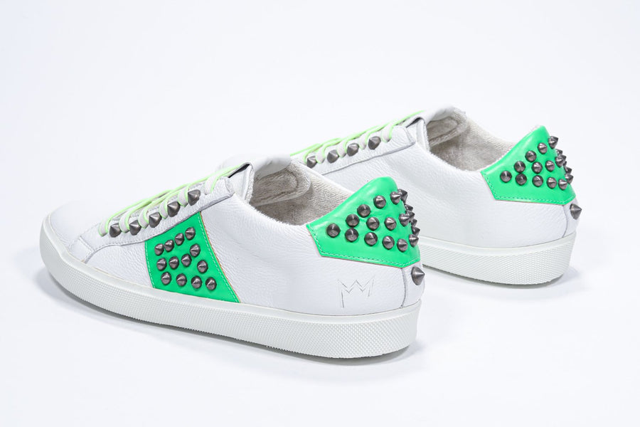 Three quarter back view of low top white and neon green sneaker. Full leather upper with studs and white rubber sole.
