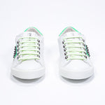 Front view of low top white and neon green sneaker. Full leather upper with studs and white rubber sole.