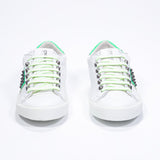 Front view of low top white and neon green sneaker. Full leather upper with studs and white rubber sole.