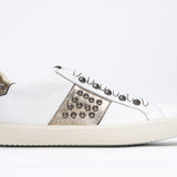 Side profile of low top white and metallic gold sneaker. Full leather upper with studs and vintage rubber sole.