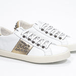Three quarter front view of low top white and metallic gold sneaker. Full leather upper with studs and vintage rubber sole.