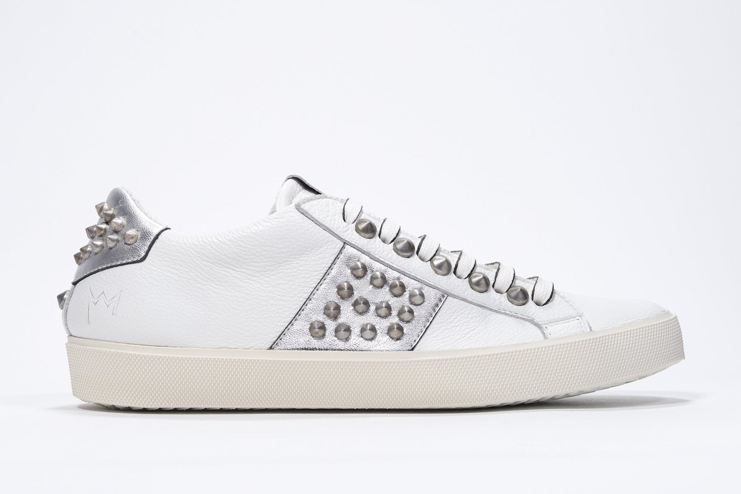 Side profile of low top white and metallic silver sneaker. Full leather upper with studs and vintage rubber sole.