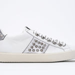 Side profile of low top white and metallic silver sneaker. Full leather upper with studs and vintage rubber sole.