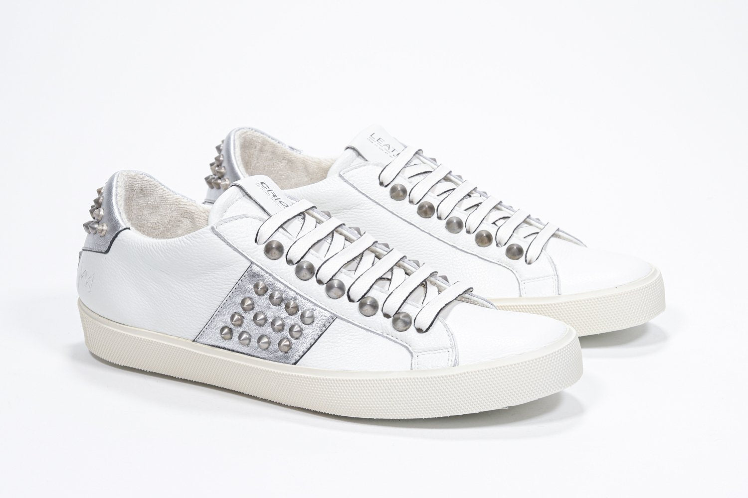 Dreiviertelansicht der Vorderseite von Low Top weiß und metallic silber sneaker. Obermaterial aus Vollleder mit Nieten und Vintage-Gummisohle.