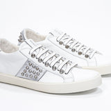 Three quarter front view of low top white and metallic silver sneaker. Full leather upper with studs and vintage rubber sole.