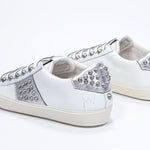 Three quarter back view of low top white and metallic silver sneaker. Full leather upper with studs and vintage rubber sole.