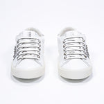 Front view of low top white and metallic silver sneaker. Full leather upper with studs and vintage rubber sole.