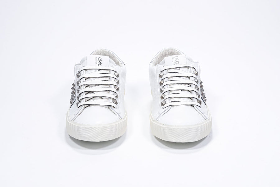 Front view of low top white and metallic silver sneaker. Full leather upper with studs and vintage rubber sole.