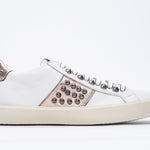 Side profile of low top white and metallic rose sneaker. Full leather upper with studs and vintage rubber sole.