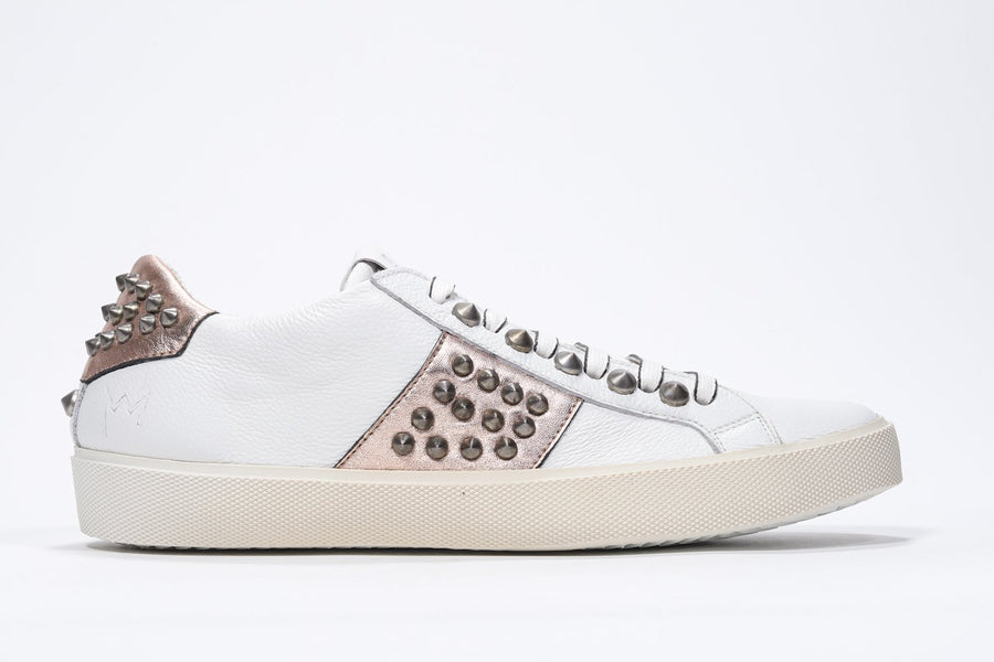 Side profile of low top white and metallic rose sneaker. Full leather upper with studs and vintage rubber sole.