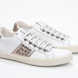 Three quarter front view of low top white and metallic rose sneaker. Full leather upper with studs and vintage rubber sole.