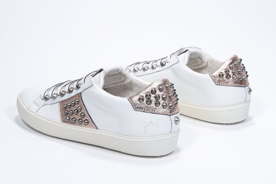 Three quarter back view of low top white and metallic rose sneaker. Full leather upper with studs and vintage rubber sole.