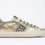 Side profile of low top metallic gold sneaker. Full leather upper with studs and vintage rubber sole.