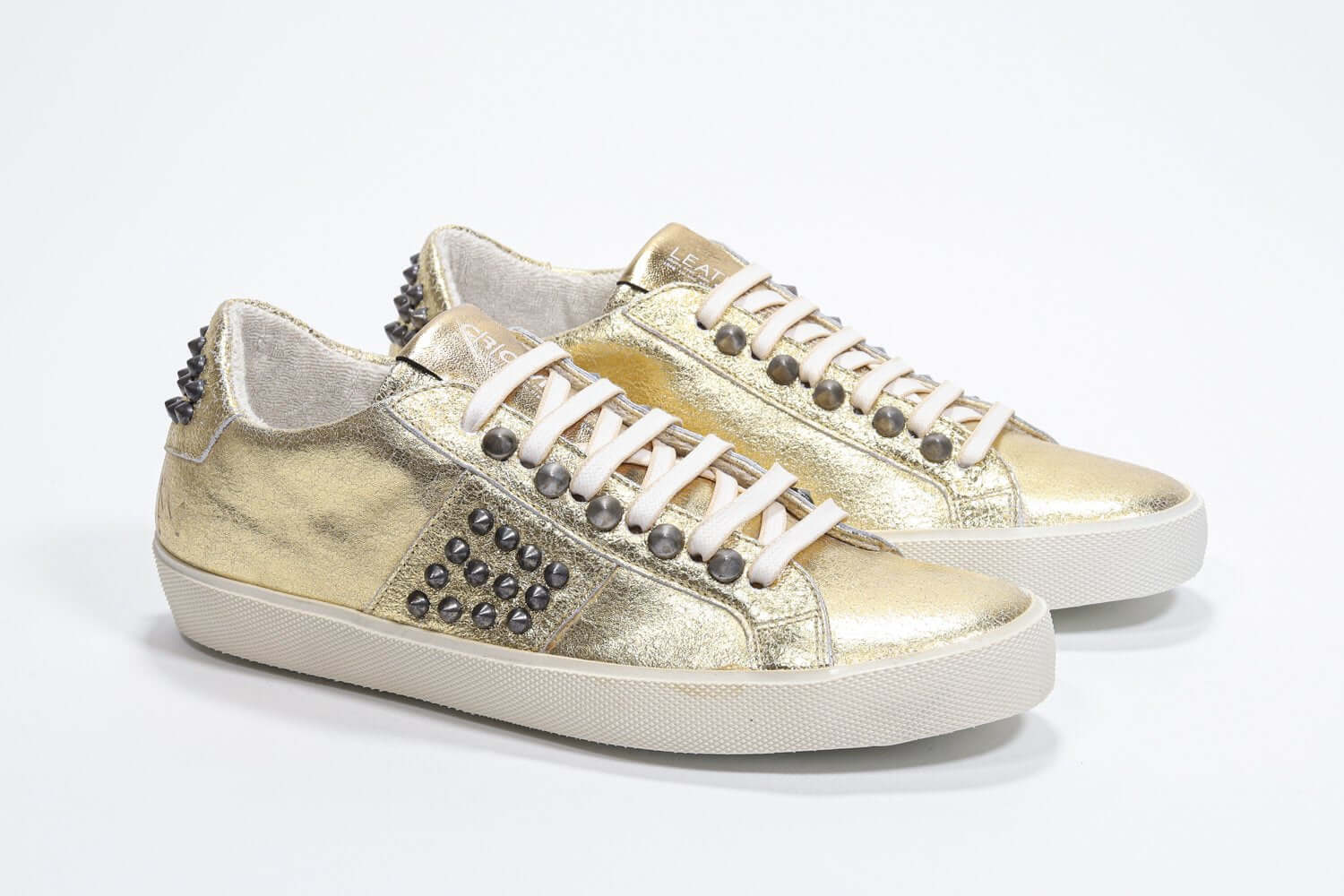 Three quarter front view of low top metallic silver sneaker. Full leather upper with studs and vintage rubber sole.