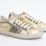 Three quarter front view of low top metallic silver sneaker. Full leather upper with studs and vintage rubber sole.