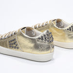 Three quarter back view of low top metallic silver sneaker. Full leather upper with studs and vintage rubber sole.