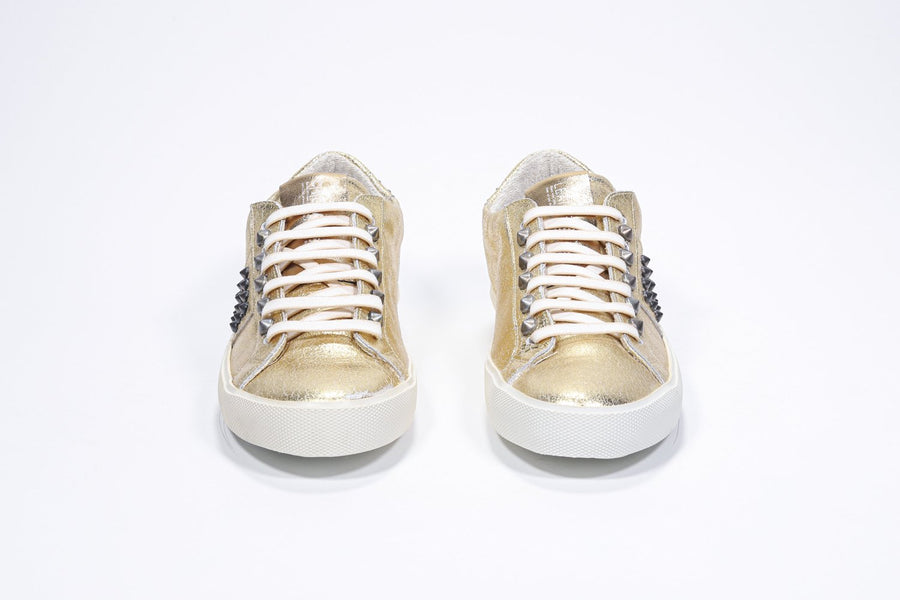 Front view of low top metallic silver sneaker. Full leather upper with studs and vintage rubber sole.