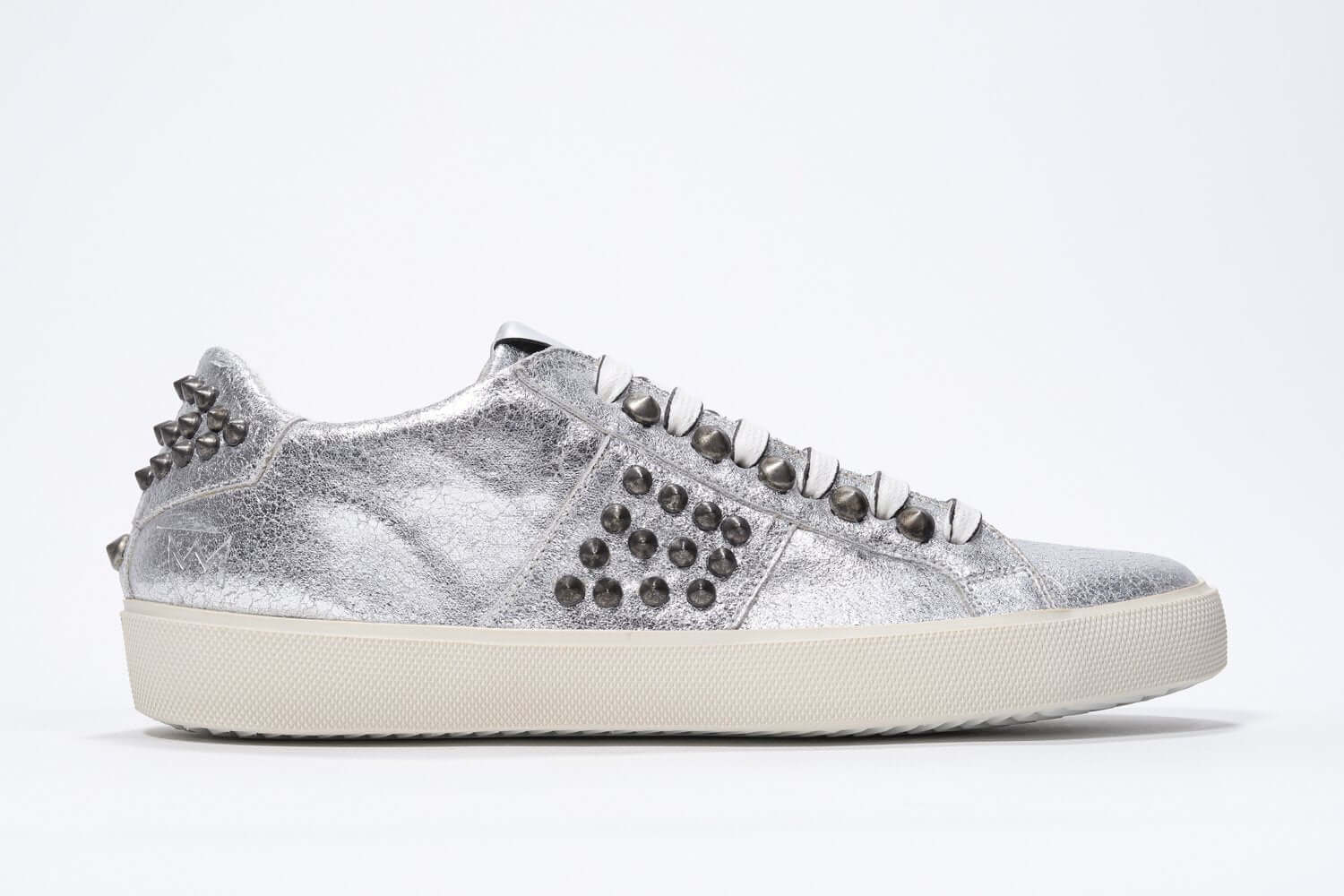Side profile of low top metallic silver sneaker. Full leather upper with studs and vintage rubber sole.