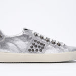 Side profile of low top metallic silver sneaker. Full leather upper with studs and vintage rubber sole.